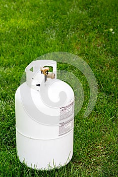 Single propane bottle sitting in the grass with warning labels
