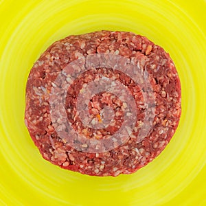 Single raw hamburger patty top view on a yellow plate