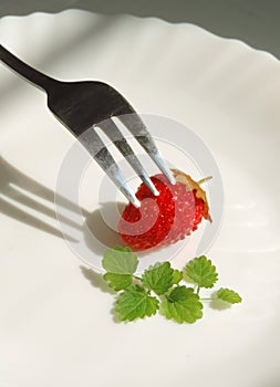 Single  ripe strawberry on a white plate with mint leaves and a fork