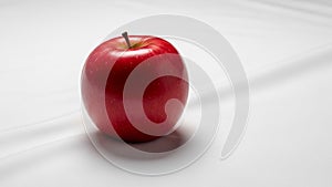 A single, red apple with a smooth, glossy surface is placed on a white fabric background. The apple