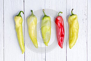 Single Red chili pepper among Green peppers on white wooden table