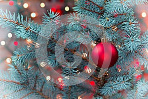 Single Red Ornament hanging from pine tree with glowing lights  in vinatage format