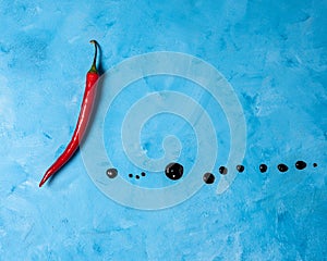 Single red pepper with aceto balsamic dots on a blue background. Top view