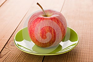 Single red striped apple in saucer on wooden table