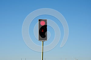 single red traffic light against a clear blue day with no vehicles