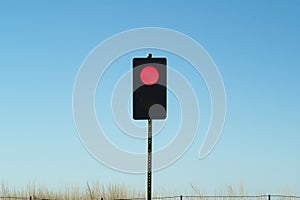 single red traffic light against a clear blue day with no vehicles