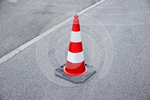Single red and white striped warning cone on gray asphalt, by day without people