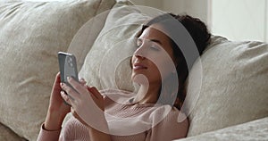 Single relaxed woman use smartphone while lying on sofa cushions