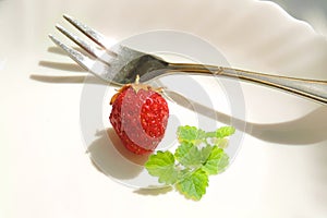 Single  ripe strawberry on a white plate with mint leaves and a fork
