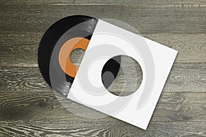 Single 45rpm vinyl record with orange label and white sleeve on wood background photo