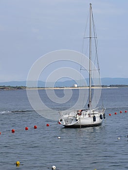 Single sailboat lies at anchor in a harbor waiting for the wind to shift . Tuscany, Italy