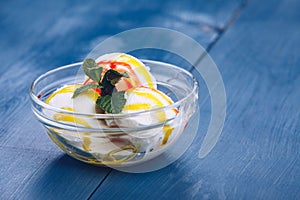 Single scoop of creamy vanilla ice cream on a stylish glass plate on a blue wooden table