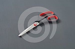 Single sharp scissors with plastic handle black and red colors lies on dark concrete desk