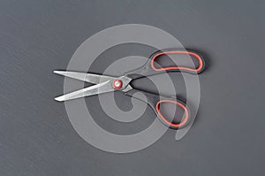 Single sharp scissors with plastic handle black and red colors lies on dark concrete desk