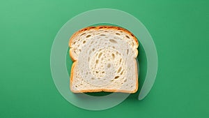 A single slice of white bread is centered on a solid green background