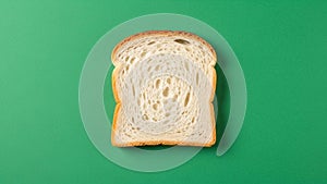 A single slice of white bread is centered on a solid green background