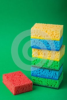 Single stack of sponges in blue, green, yellow colors near one red sponge on green paper background