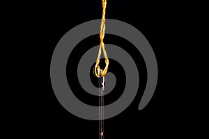 A single Steel sewing needle threaded with a vivid yellow thread  on a black background ready to be used in crafts and garment