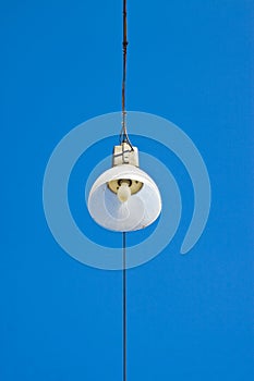 Single streetlight hanging from a metal cable on a blue background