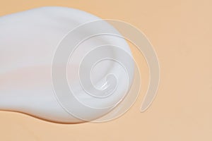 A single stroke of white cosmetic cream on a beige background, ideal for skincare and beauty concepts. Macro with copy