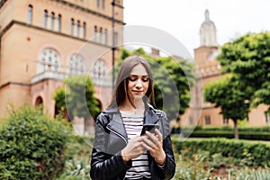 Single student walking and reading mobile phone messages with a university building in the background