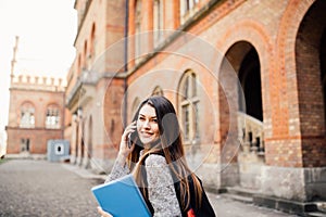 Single student walking and speak mobile phone with a university building in the background