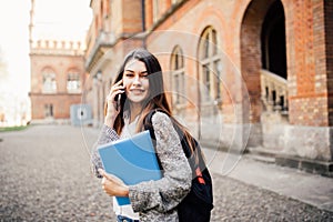 Single student walking and speak mobile phone with a university building in the background