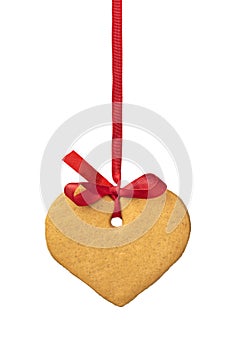 Single sweet cookie in heart shape hanging on a red ribbon on white background