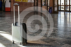Single unattended trolley wheeled suitcase on stone floor in empty train station hall