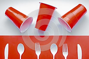 Single use white plastic cutlery and red plastic glass on a red and white background. Concept: Ban single use plastic