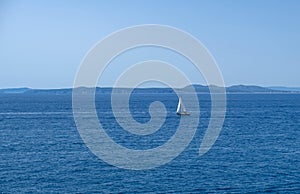 Single white boat sailing on calm water in a sunny day along the coast