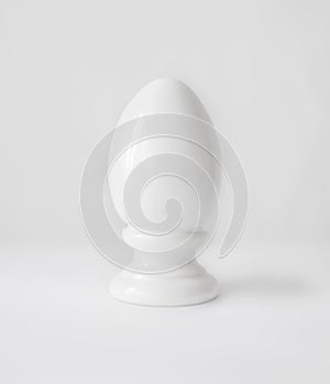 Single white decorative ceramic statuette egg in egg-cup on white table top background. Easter religious Christian symbol.