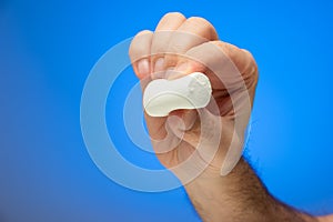 Single white marshmallow held between fingers by Caucasian male hand isolated against blue background studio shot close up