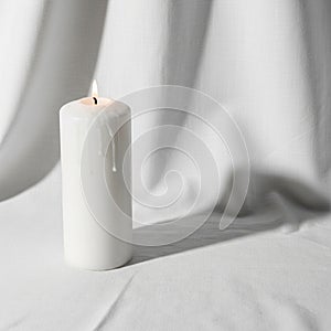 A single white pillar candle stands lit on a white fabric drape