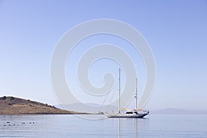 A single white sailing boat in blue aegean sea with mountain and sky in background, with copy space