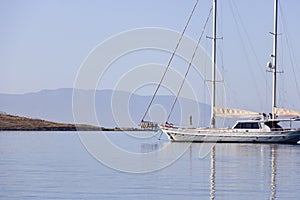 A single white sailing boat in blue aegean sea with mountain and sky in background, with copy space