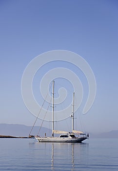 A single white sailing boat in blue aegean sea with mountain and sky in background, with copy space