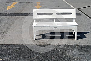 single white wooden bench is placed in afternoon sunlight on concrete floor of empty parking lot