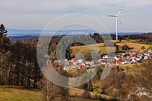 A single wind turbine on a hill above a village with the distant skyline of Frankfurt