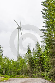 Single Wind Turbine in the middle of the green forest under blue sky with clouds. Windfarm, wind power plant