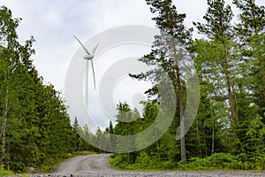 Single Wind Turbine in the middle of the green forest under blue sky with clouds. Windfarm, wind power plant