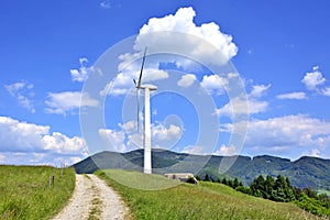 A single windmill in the  foreground against a blue   sky with white clouds