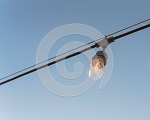 Single wired Illuminated bulb on clear blue sky background at backyard decoration