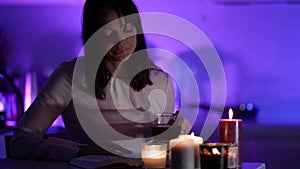 Single woman is drinking tea and reading book at home at night, romantic candle light