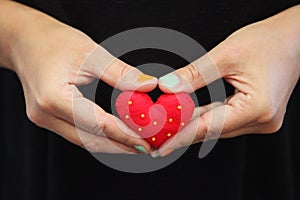 A single woman with her hands together holding a red felted heart