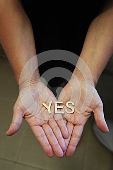 A single woman with her hands together with wooden letters forming the word Yes