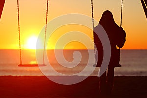 Single woman sitting on a swing contemplating sunset