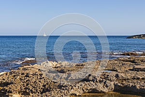 SIngle yacht oon blue sea with rocky beach