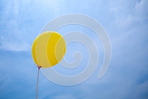 Single yellow balloon under cloudy sky. hand holds the balloon rope up to the sky.
