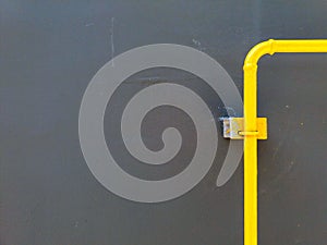 Single yellow gas, oil, PVC or water pipeline on gray or black wall